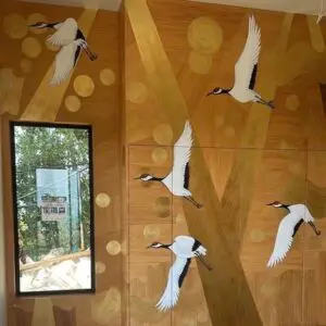 Interior mural in London with flying white cranes, and golden accents on a wood-textured background