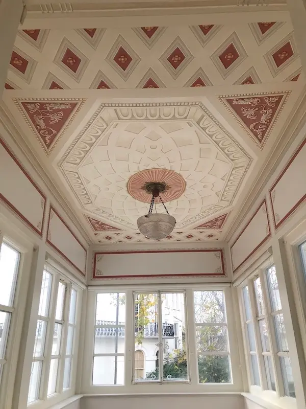 A sunroom featuring a white ceiling adorned with trompe l'oeil painting, creating an illusion of depth and dimension.