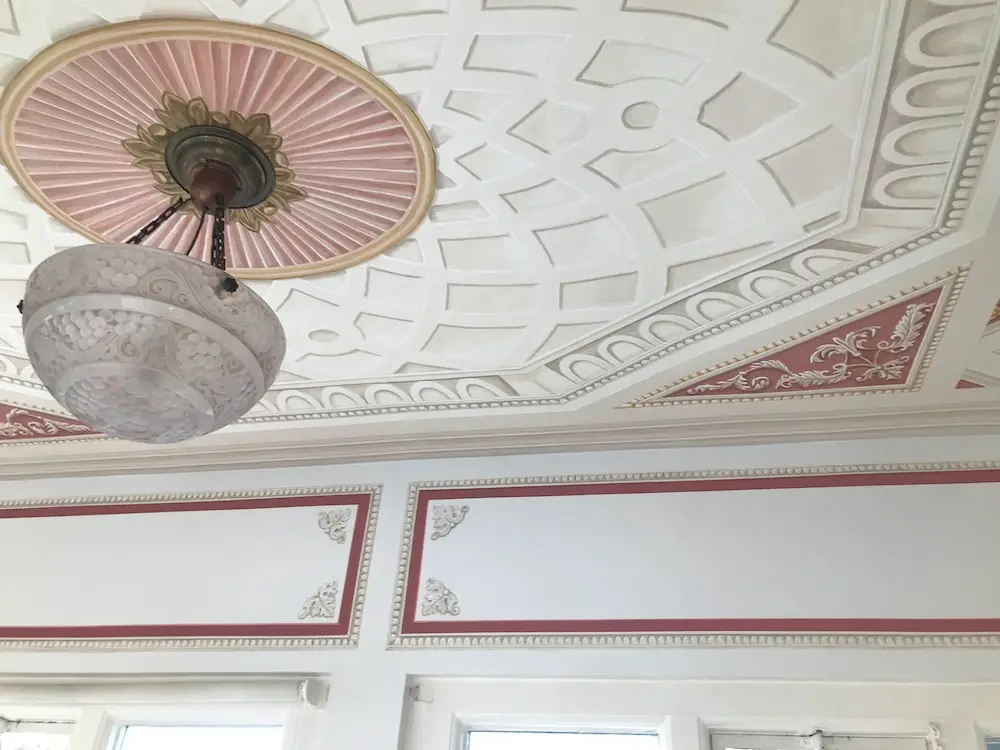 Ornate ceiling featuring trompe l'oeil painting and an elegant chandelier hanging in the center.