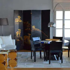 A stylish living room featuring a table, chairs, and a black and gold oriental screen, showcasing elegant decor.