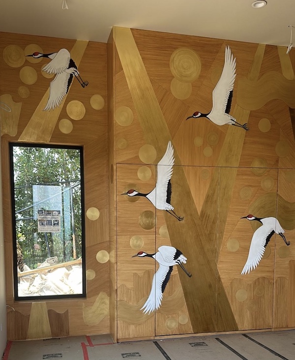 Interior mural in London with flying white cranes, and golden accents on a wood-textured background