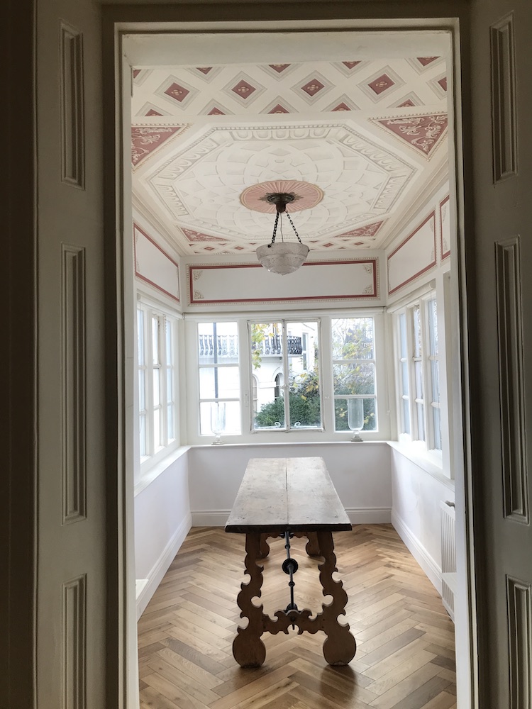 A room featuring a table and a trompe l'oeil patterned ceiling